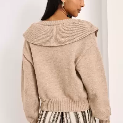 Mulher de costas com camisola de malha bege e calças às riscas verticais.