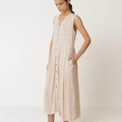 Vestido comprido bege com padrão geométrico castanho e botões dourados, usado por mulher com sandálias castanhas