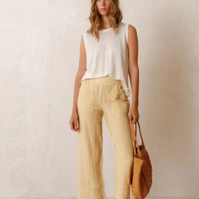 Mulher com calças xadrez amarelas e branca, camisa branca e bolsa de palha