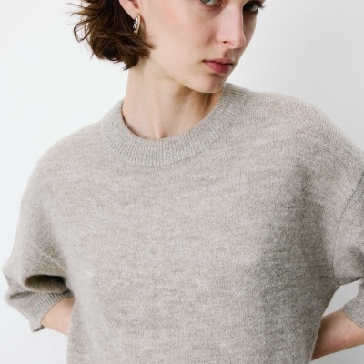 Pessoa com camisola cinzenta de malha e brincos de argola prateados.