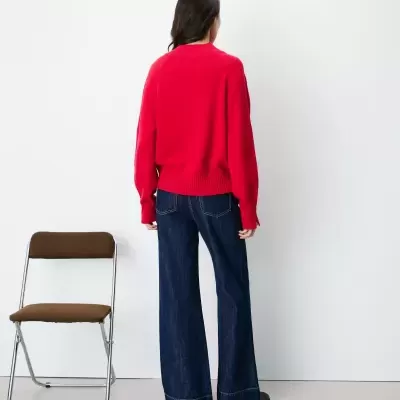 Pessoa de costas com camisola vermelha e calças de ganga largas ao lado de cadeira castanha.
