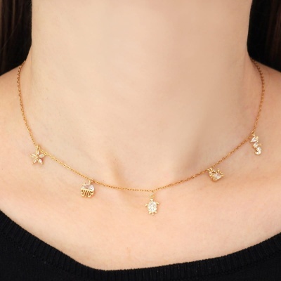 Colar fino dourado com cinco pequenos pendentes diferentes num pescoço com camisola preta