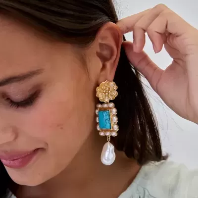 Brinco pendente dourado com pedra azul e pérolas usado por mulher