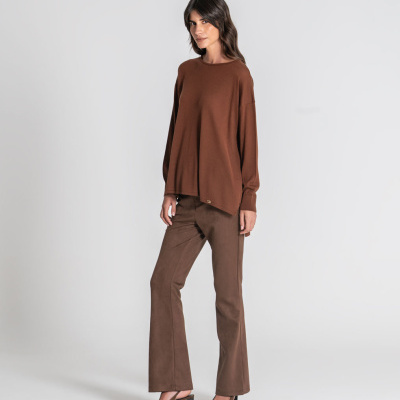 Conjunto de roupa feminina castanha com camisola, calças e sapatos, fundo branco.