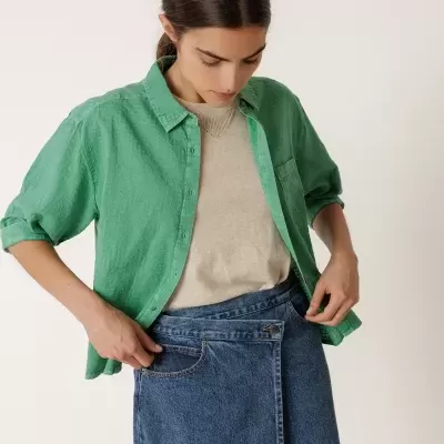 Mulher com camisa verde, camisola bege e saia midi de ganga azul
