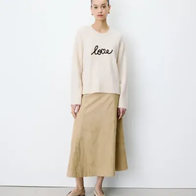 Mulher com camisola bege de malha com a palavra love e saia midi bege.