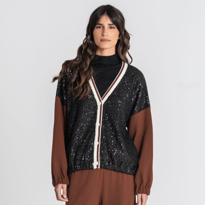 Cardigan preto com lantejoulas e botões brancos usado com camisa preta de gola alta e calças castanhas