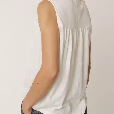 Top branco sem mangas com pregas na parte de trás e calças azul escuro às riscas