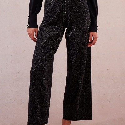 Calças pretas com brilhos dourados e cordão na cintura vistas em fundo neutro