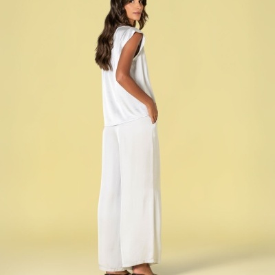 Conjunto feminino branco com top sem mangas e calças largas, sapatos pretos de salto baixo, fundo amarelo.