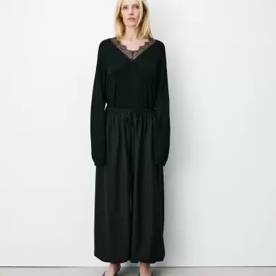 Mulher com blusa preta com decote em renda e calças largas pretas