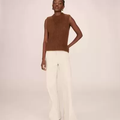 Mulher com camisola castanha sem mangas e calças brancas.