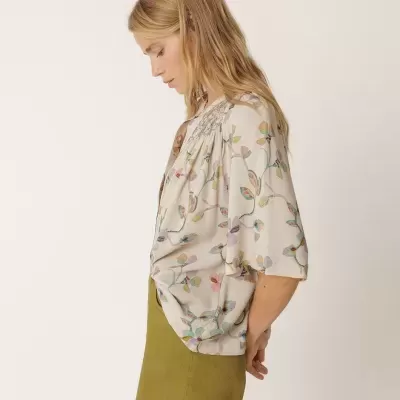 Mulher de perfil com blusa floral branca e saia verde-oliva