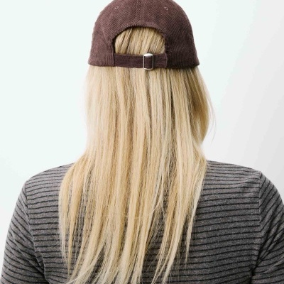 Pessoa vista de costas com boné castanho de tecido e t-shirt cinza às riscas