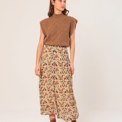 Mulher usando colete castanho de malha, saia comprida estampada floral, e botas castanhas