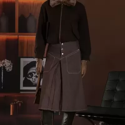 Mulher com casaco preto com gola de pelo castanho e saia midi castanha, botas altas castanhas, luvas castanhas e chapéu bege com padrão