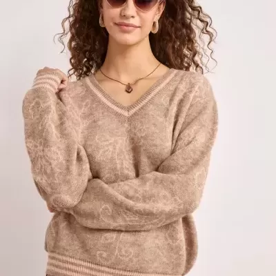 Camisola bege com padrão subtil e saia floral rosa em mulher com cabelo encaracolado.