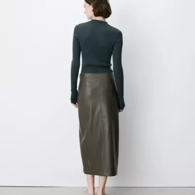 Mulher de costas com camisola cinzenta e saia de couro castanha