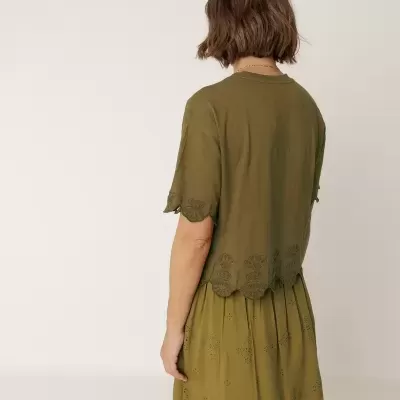 Pessoa de costas com vestido verde bordado em fundo neutro