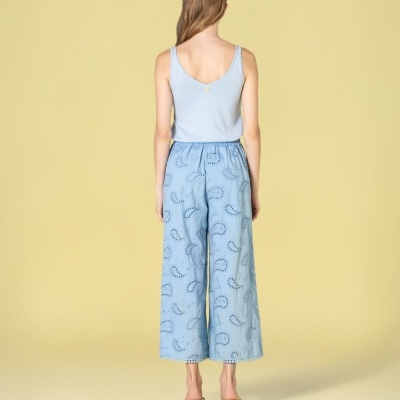 Mulher de costas com calças largas azuis claras com padrão calado e top azul claro, sandálias pretas com salto.