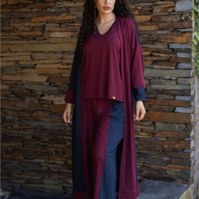 Mulher a usar conjunto desportivo vinho e azul escuro junto a parede de pedra