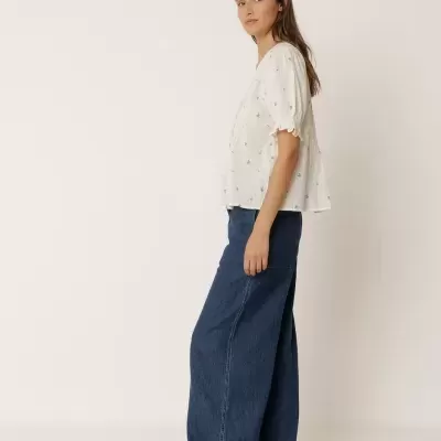 Blusa branca manga curta com detalhes dourados e saia/calça jeans azul largo