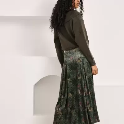 Mulher de costas com camisola castanha e saia padrão folhas verde