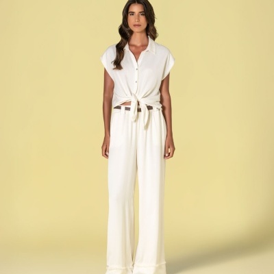 Mulher com conjunto branco de camisa sem mangas e calças largas em fundo amarelo claro.