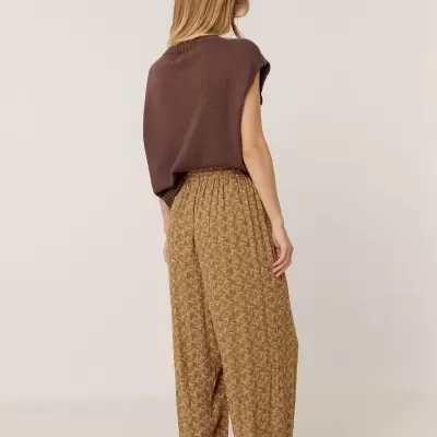 Mulher de costas com colete castanho e calças largas castanhas com padrão floral.