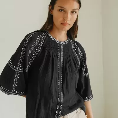 Blusa preta bordada com calças bege claras em fundo neutro.