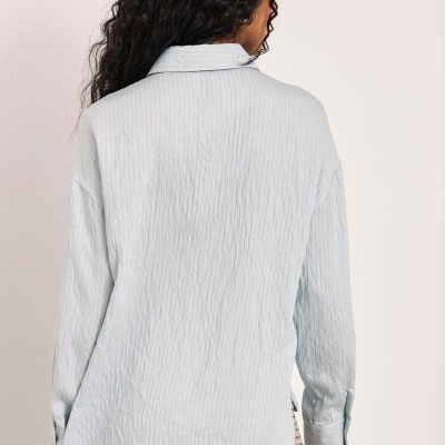 Pessoa de costas com camisa azul clara texturizada e saia bege xadrez