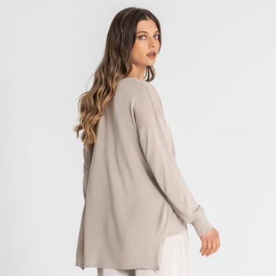 Mulher com camisola bege de malha comprida e calças brancas