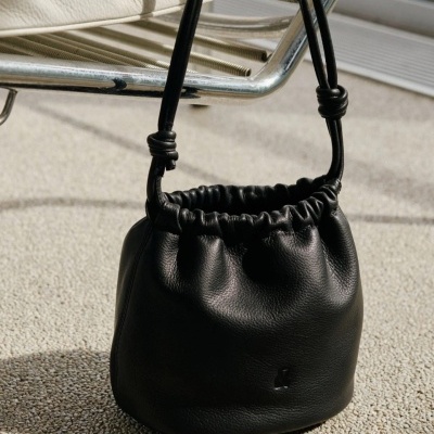 Saco preto de couro sintético com alça e textura franzida perto de cadeira