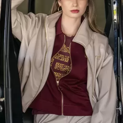 Mulher com fato de treino bege, camisola borgonha e boné bege com letra J sentada num carro