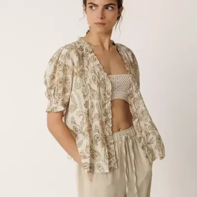 Mulher a usar blusa floral aberta, top de croché e pantalonas bege