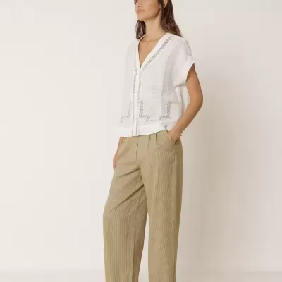 Mulher com blusa branca e calças cinza com riscas em fundo neutro