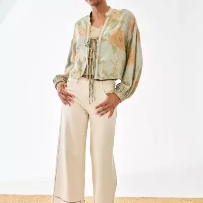 Pessoa com roupa casual floral e calças largas claras em fundo branco e tapete ráfia