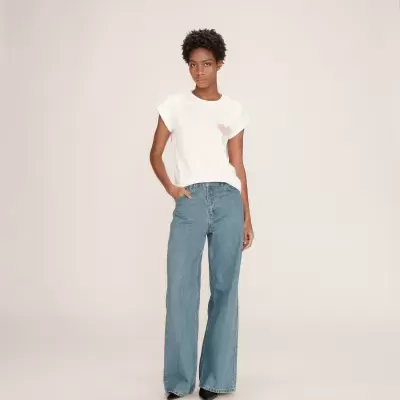 Mulher a usar t-shirt branca com coração rosa e calças de ganga largas azuis.