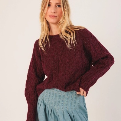 Mulher com camisola bordô e saia azul claro num fundo branco.