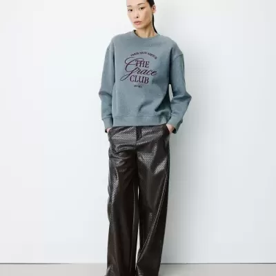 Mulher com sweatshirt cinza e calças largas castanho-escuro em fundo branco