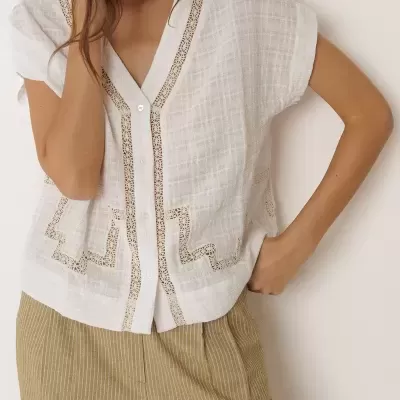 Blusa branca feminina com botões e detalhes rendados, combinada com calças bege de risca de giz