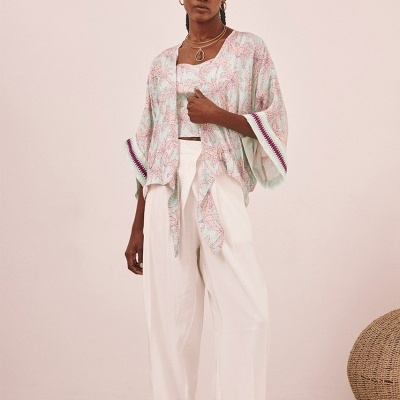 Mulher vestindo colete e camisa floral clara com calças brancas e sandálias,cenário interior minimalista