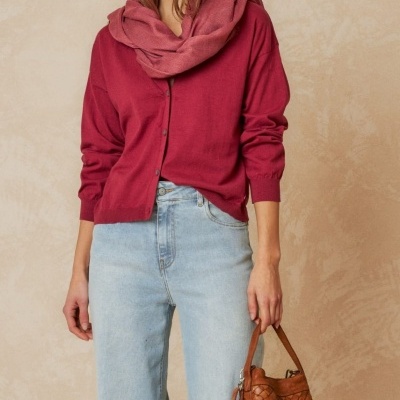 Mulher com casaco grená, lenço rosa, calças de ganga azul claro e mala castanha de couro entrelaçado