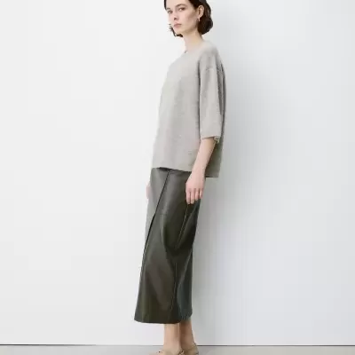 Mulher com camisola cinza clara de malha e saia preta comprida com sapatos bege