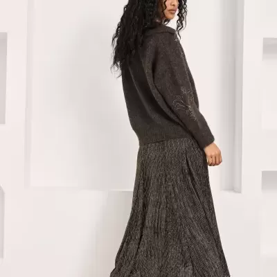 Mulher de costas com camisola preta de malha e saia longa plissada preta e cinza