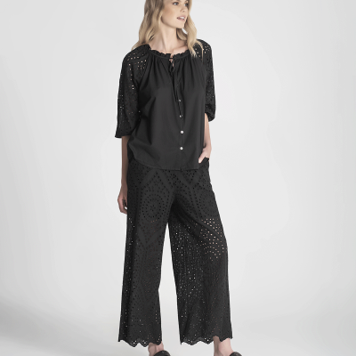 Conjunto feminino preto com blusa e calças largas vazadas, sandálias pretas, fundo cinza.