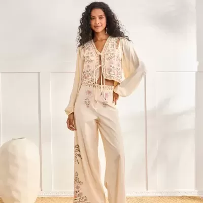 Macacão comprido creme com bordados florais e mangas compridas junto a vaso creme