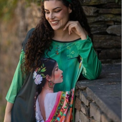 Mulher com túnica colorida estampada, faixa verde no cabelo, encostada num muro de pedra