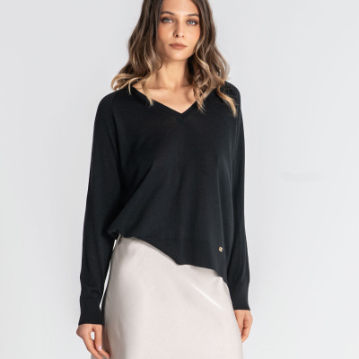 Mulher com camisola preta de malha com decote em V e saia creme com renda preta.