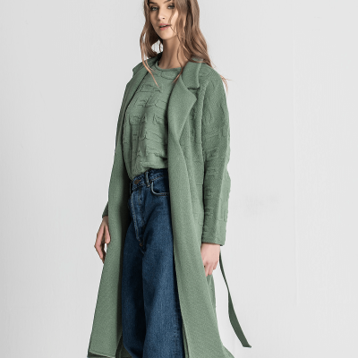 Mulher com casaco longo e camisola verde clara e calças jeans azuis